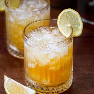 Maple Whiskey Sour's in glasses with lemon slides on a wooden table.