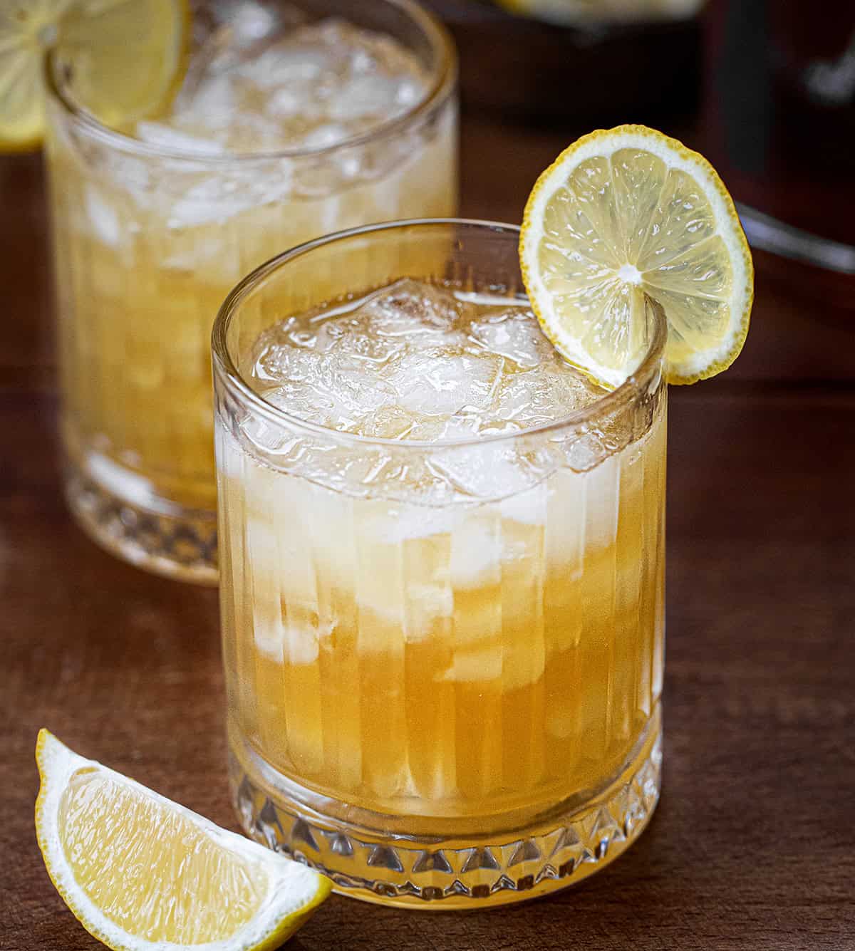 Maple Whiskey Sour's in glasses with lemon slides on a wooden table.
