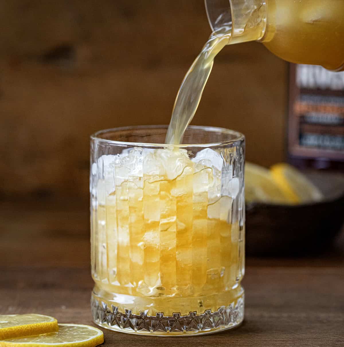 Pouring Maple Whiskey Sour into a glass filled with ice.