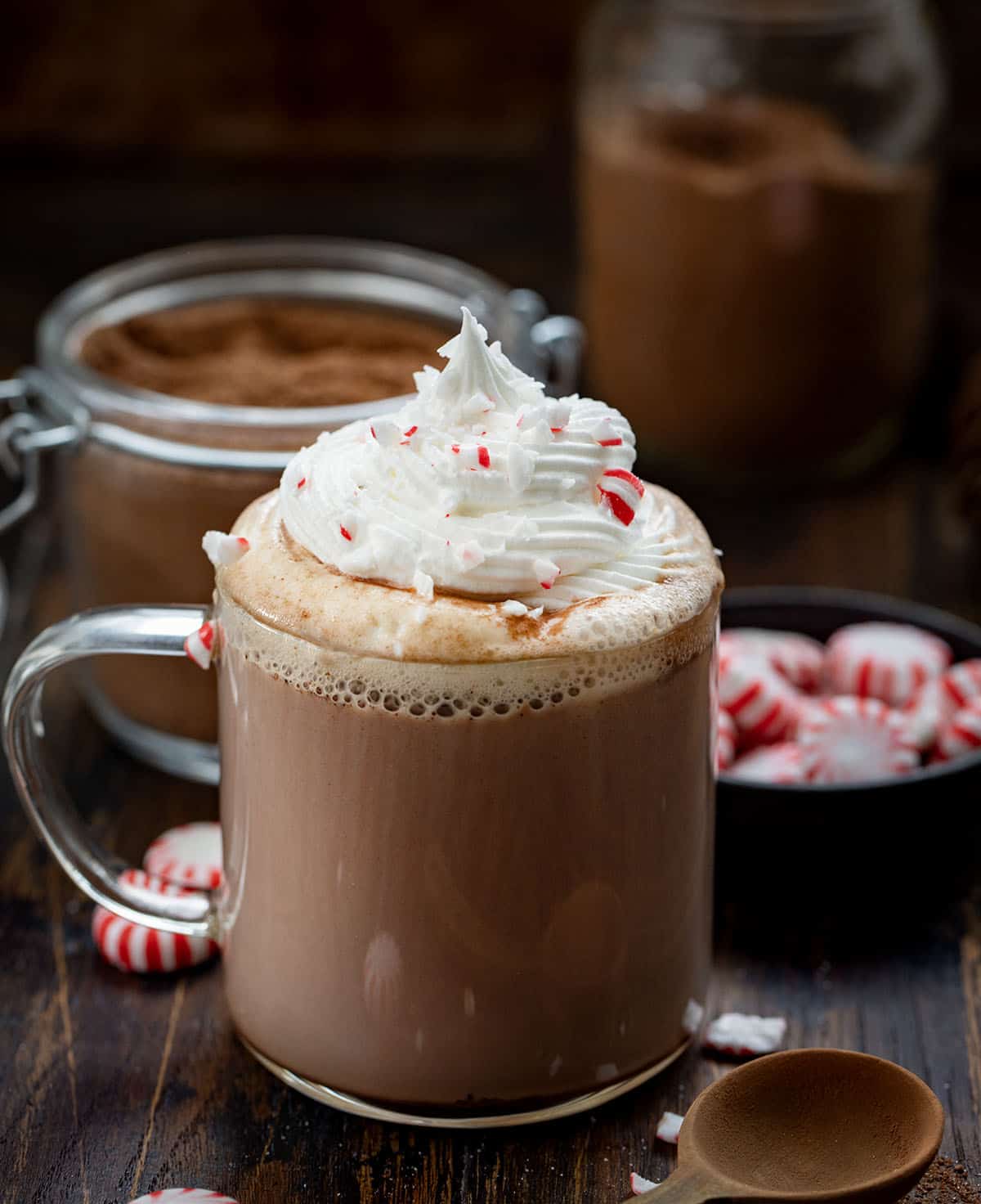 Nothing says cozy winter nights like a mug of rich, creamy hot chocolate with a hint of peppermint. This Peppermint Hot Cocoa Mix is easy to make ahead, customizable, and perfect for gifting during the holidays. Each sip delivers a smooth chocolate flavor with a refreshing minty finish! Glass of Peppermint Hot Cocoa in front of Peppermint Hot Cocoa Mix on a wooden table.