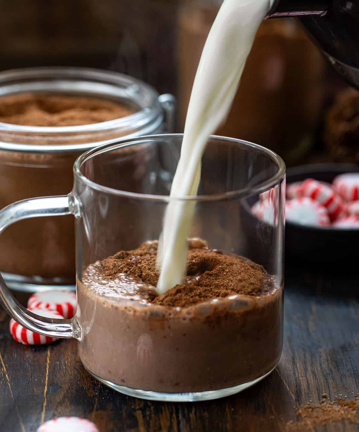 Nothing says cozy winter nights like a mug of rich, creamy hot chocolate with a hint of peppermint. This Peppermint Hot Cocoa Mix is easy to make ahead, customizable, and perfect for gifting during the holidays. Each sip delivers a smooth chocolate flavor with a refreshing minty finish! Pouring milk into a glass mug filled with Peppermint Hot Cocoa Mix.