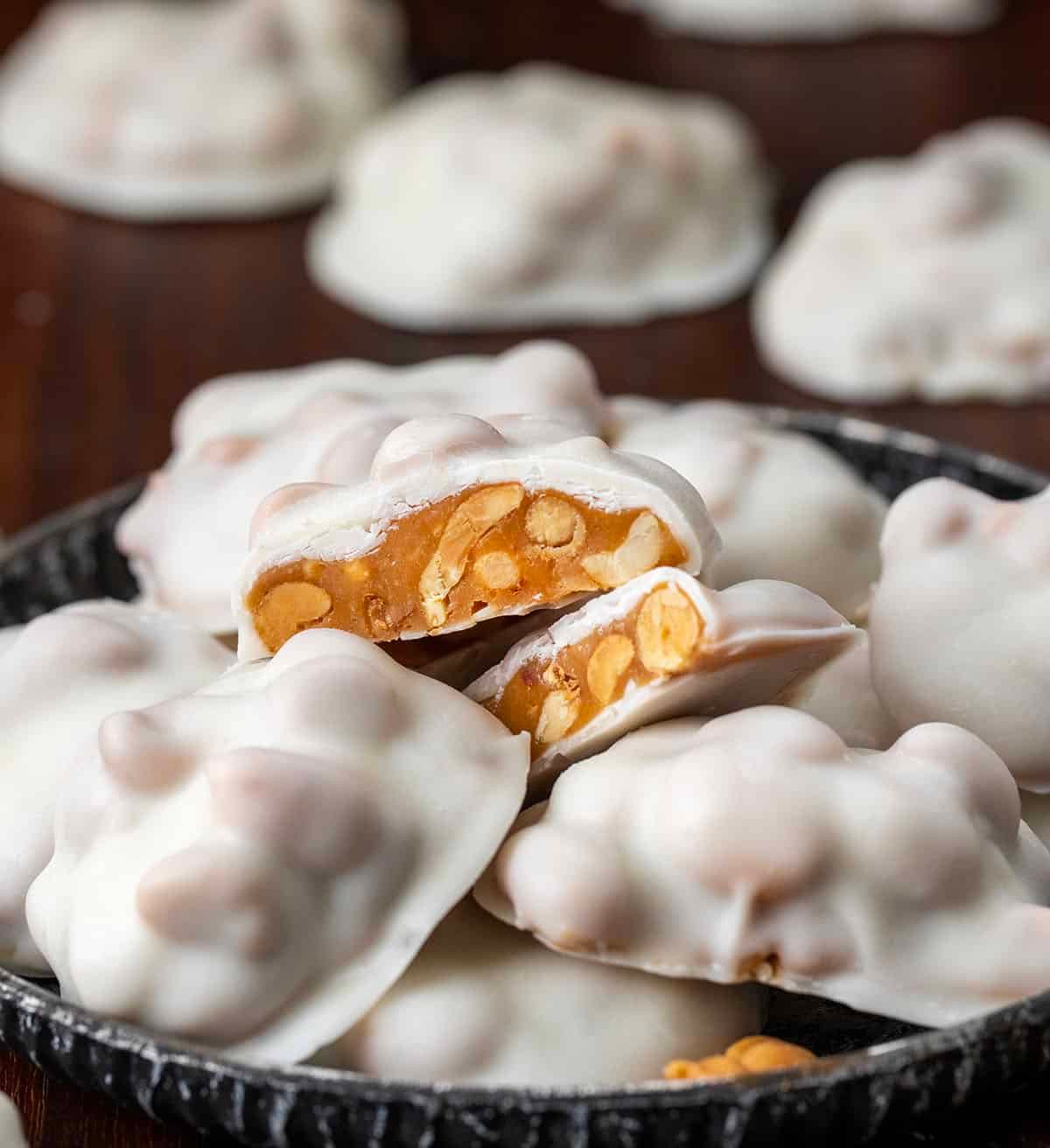 If you love sweet and salty treats, Polar Bear Paws are the perfect candy to make this holiday season. These bite-sized clusters combine crunchy roasted peanuts, gooey caramel, and smooth vanilla almond bark for a candy thatโs irresistible to snack on! Polar Bear Paws candy on a plate with one piece cut in half.