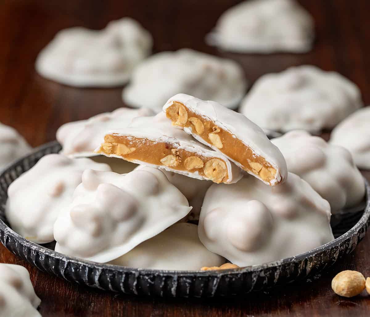 If you love sweet and salty treats, Polar Bear Paws are the perfect candy to make this holiday season. These bite-sized clusters combine crunchy roasted peanuts, gooey caramel, and smooth vanilla almond bark for a candy thatโs irresistible to snack on! Polar Bear Paws on a mini platter on a wooden table with one piece cut in half.
