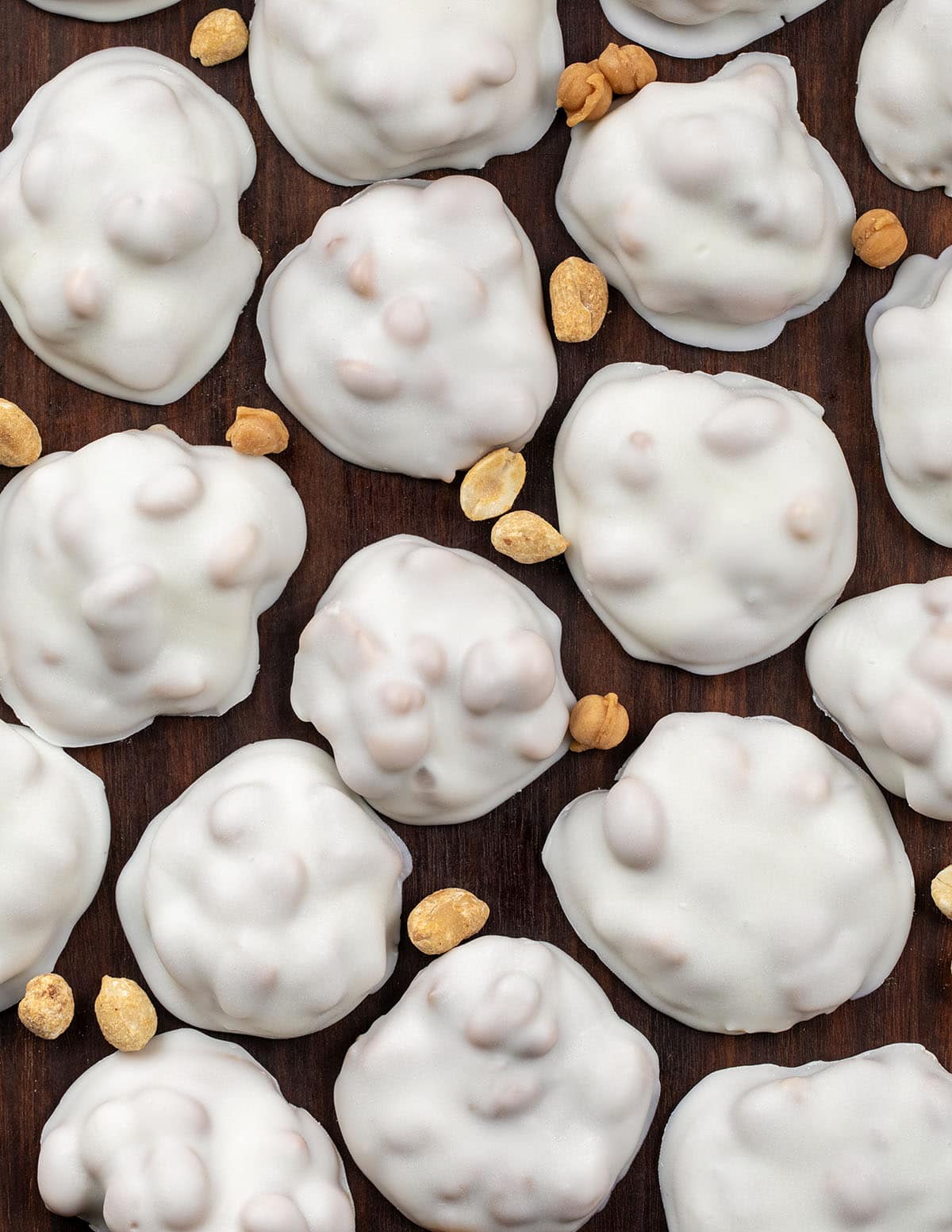 If you love sweet and salty treats, Polar Bear Paws are the perfect candy to make this holiday season. These bite-sized clusters combine crunchy roasted peanuts, gooey caramel, and smooth vanilla almond bark for a candy thatโs irresistible to snack on! Polar Bear Paws spread out on a wooden table with peanuts from overhead.