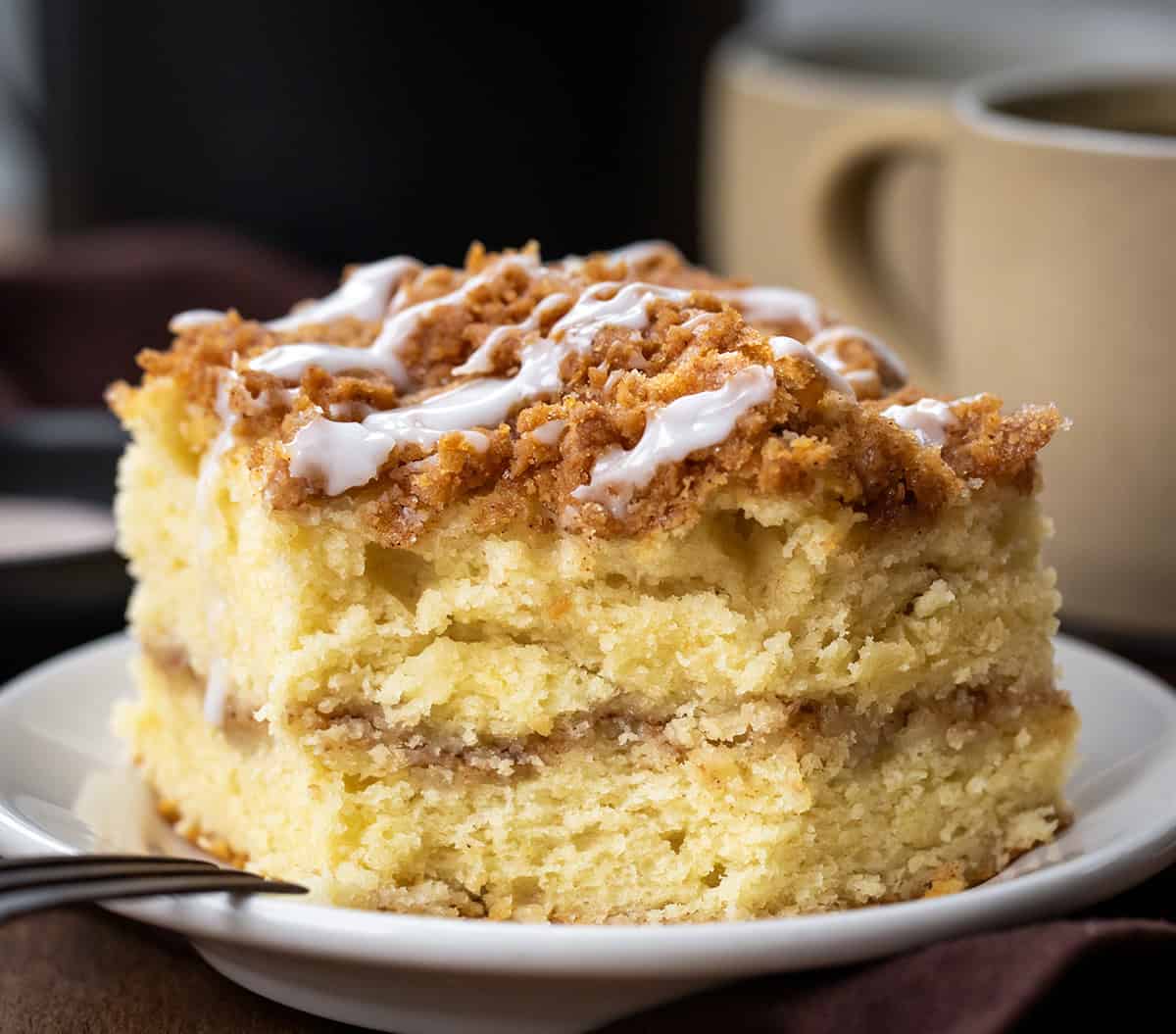 Piece of Snickerdoodle Coffee Cake on a white plate with a bite removed showing the tender crumb and cinnamon swirl.