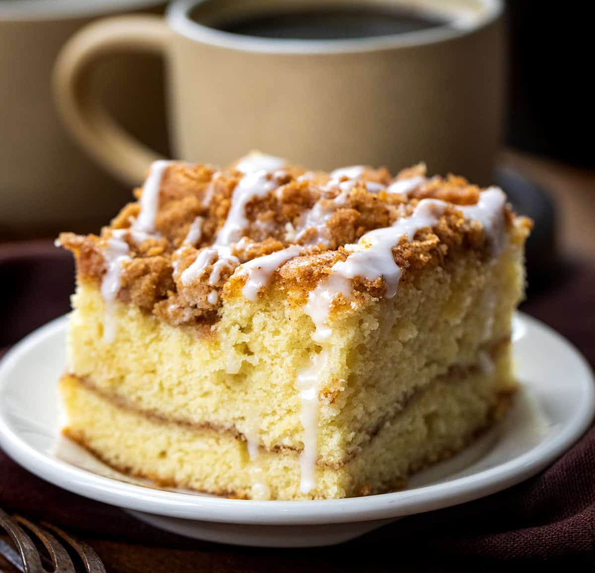 If you love snickerdoodles, wait until you try them in coffee cake form! This Snickerdoodle Coffee Cake combines the buttery cinnamon-sugar goodness of the classic cookie with a soft, tender cinnamon coffee cake! Piece of Snickerdoodle Coffee Cake on a white plate with coffee cups on a wooden table.