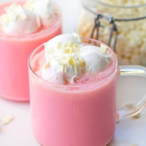 Glasses of Strawberry Hot Chocolate on a white table with white chocolate chips.