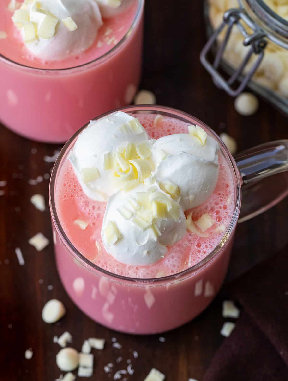 Glasses of Strawberry Hot Chocolate on a wooden table with white chocolate chips.