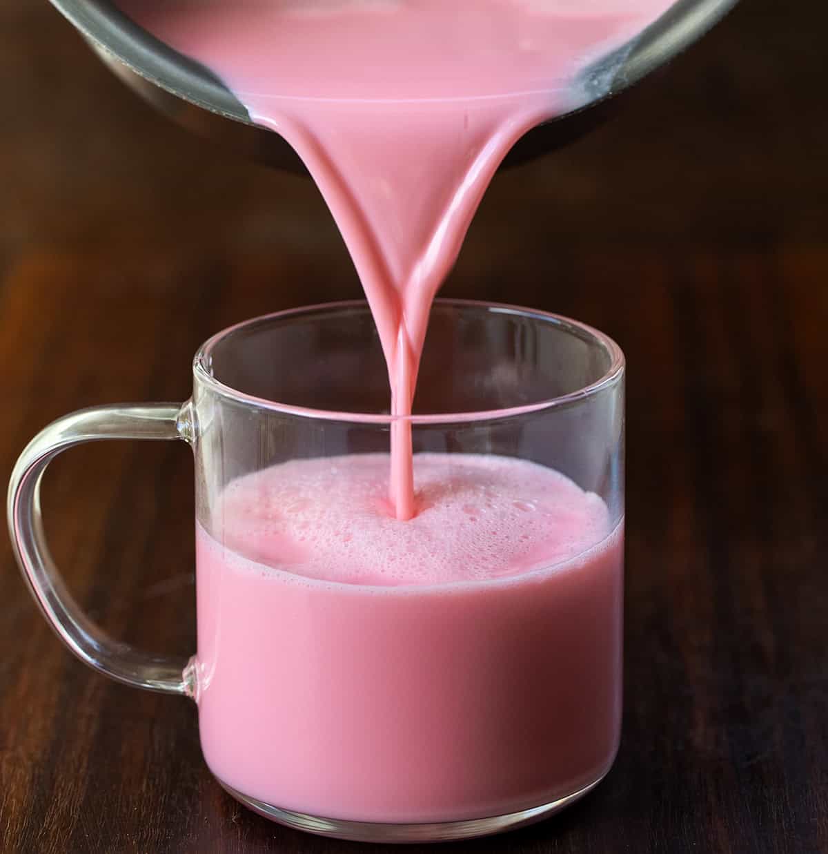 Pouring Strawberry Hot Chocolate from the pot into a glass mug.