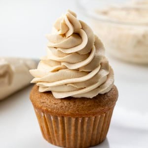 Cupcake with Brown Sugar Ermine Frosting piped on it with piping bag and bowl of ermine in the background.