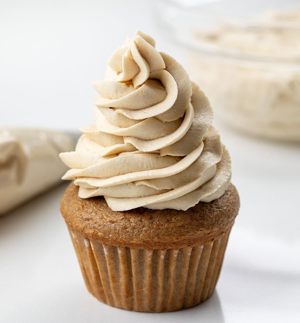 Cupcake with Brown Sugar Ermine Frosting piped on it with piping bag and bowl of ermine in the background.