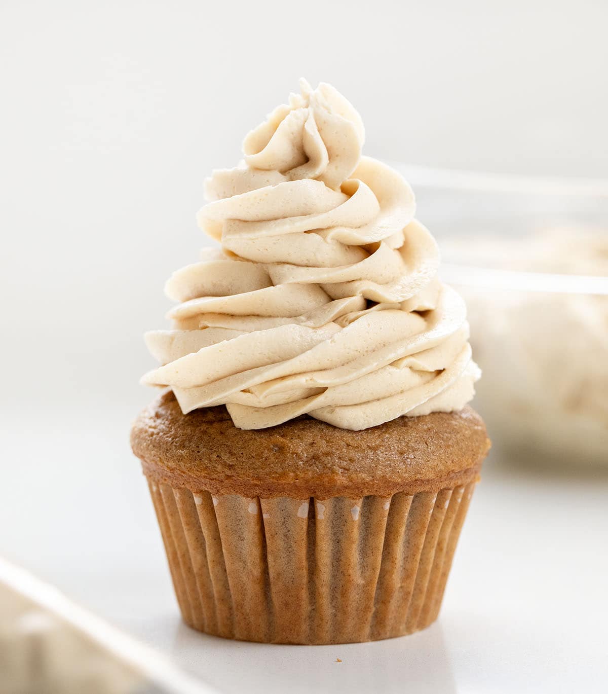 Cupcake with Brown Sugar Ermine Frosting piped on it with piping bag and bowl of ermine in the background.