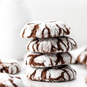 Stack of Chocolate Peppermint Crinkle Cookies on a white table with milk in the background.