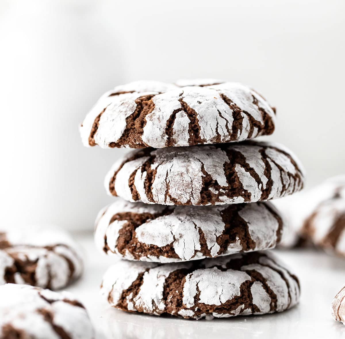 Stack of Chocolate Peppermint Crinkle Cookies on a white table with milk in the background.
