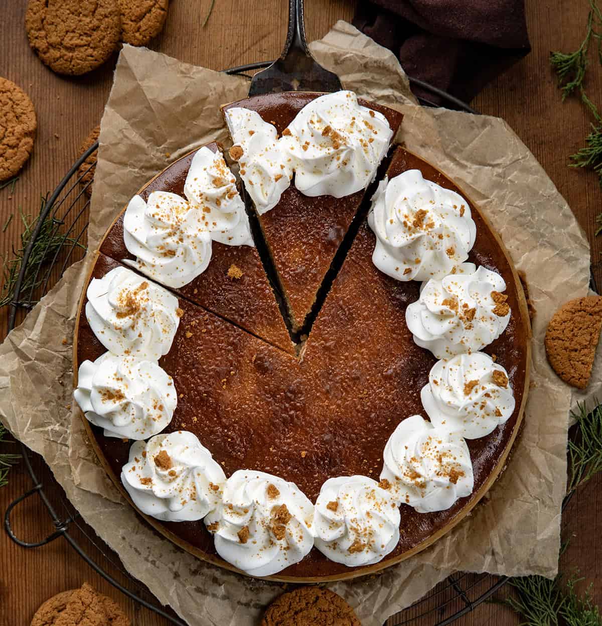 Gingerbread Cheesecake on a rack with brown parchment paper with a couple of sliced cut and one about to be removed with a cake server.