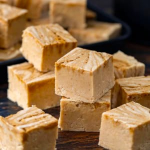 Stack of Gingerbread Fudge next to many other square fudge pieces on a wooden table.