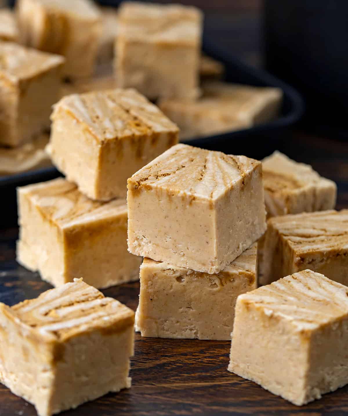 Stack of Gingerbread Fudge next to many other square fudge pieces on a wooden table.