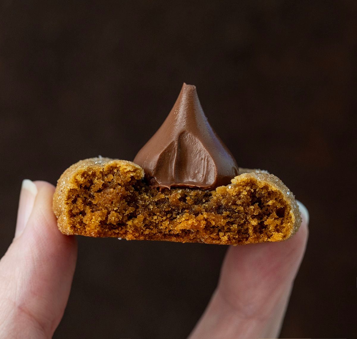 Hand holding a bit into Gingerbread Kiss Cookie.