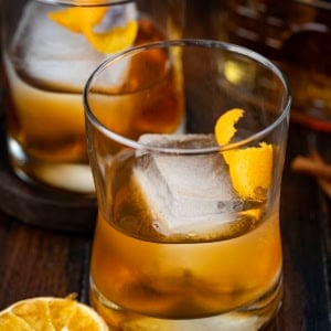 Glasses of Maple Old Fashioned on a wooden table with dried oranges and bourbon.