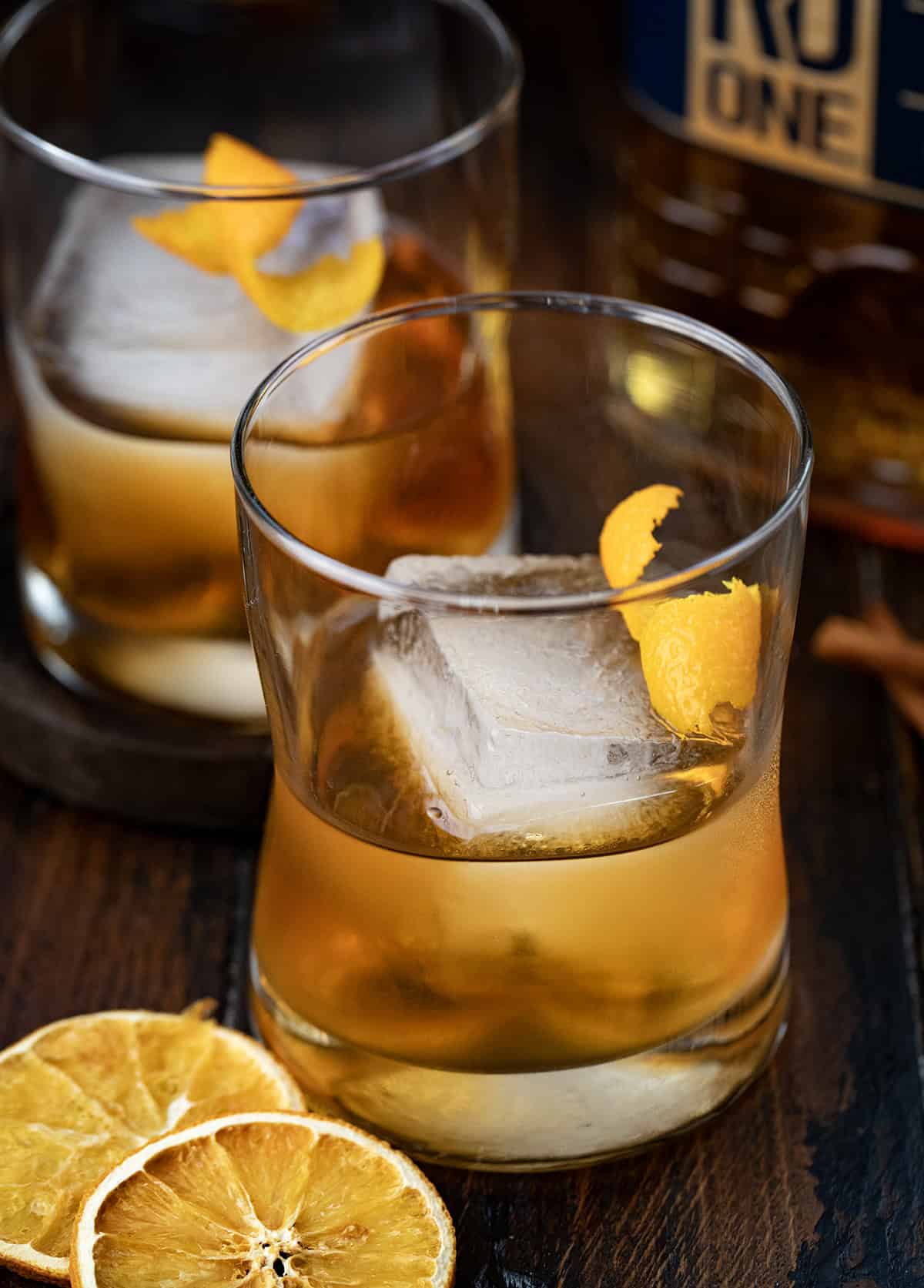 Glasses of Maple Old Fashioned on a wooden table with dried oranges and bourbon.