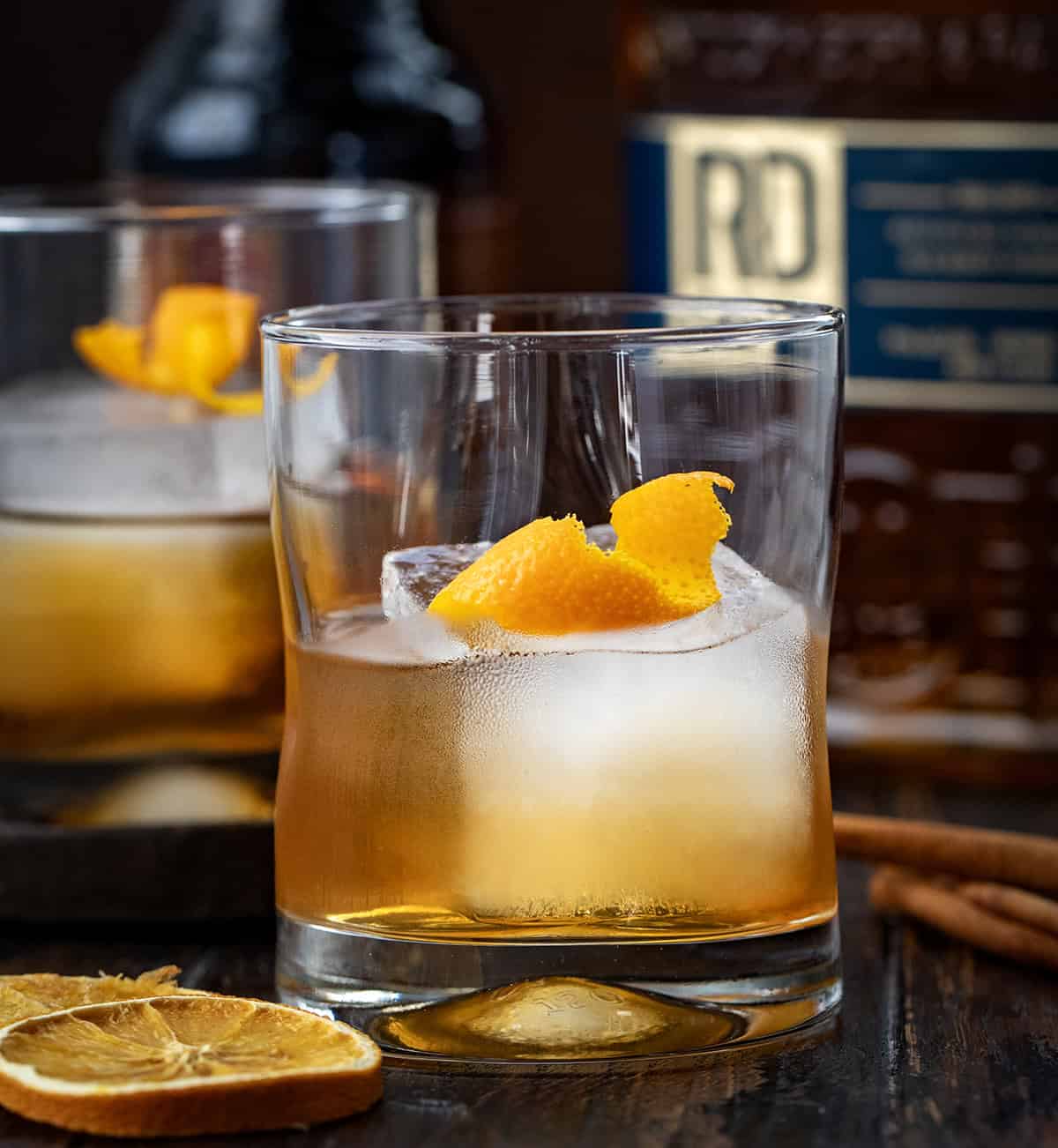 Warm, cozy, and perfectly spiced for fall, this Maple Old Fashioned is a classic cocktail with a seasonal twist! Whether you’re winding down after a busy day or serving a cocktail at a cool-weather gathering, this drink is easy to make and sure to impress! Close up of a glass of Maple Old Fashioned with an orange twist.