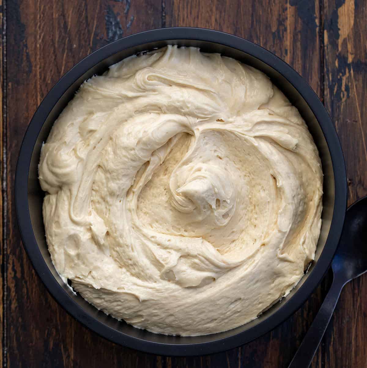 Rich, creamy, and perfectly spiced, this Molasses Cream Cheese Frosting adds cozy holiday flavor to any dessert. The tangy cream cheese pairs beautifully with the deep sweetness of molasses for a frosting that tastes like gingerbread in creamy form! Black bowl filled with Molasses Cream Cheese Frosting on a wooden table from overhead.
