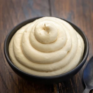 Molasses Cream Cheese Frosting piped into a black bowl on a wooden table.