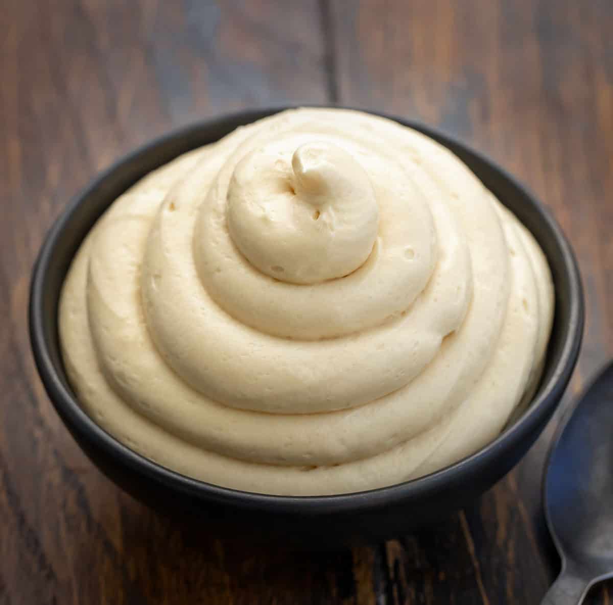 Rich, creamy, and perfectly spiced, this Molasses Cream Cheese Frosting adds cozy holiday flavor to any dessert. The tangy cream cheese pairs beautifully with the deep sweetness of molasses for a frosting that tastes like gingerbread in creamy form! Molasses Cream Cheese Frosting piped into a black bowl on a wooden table.