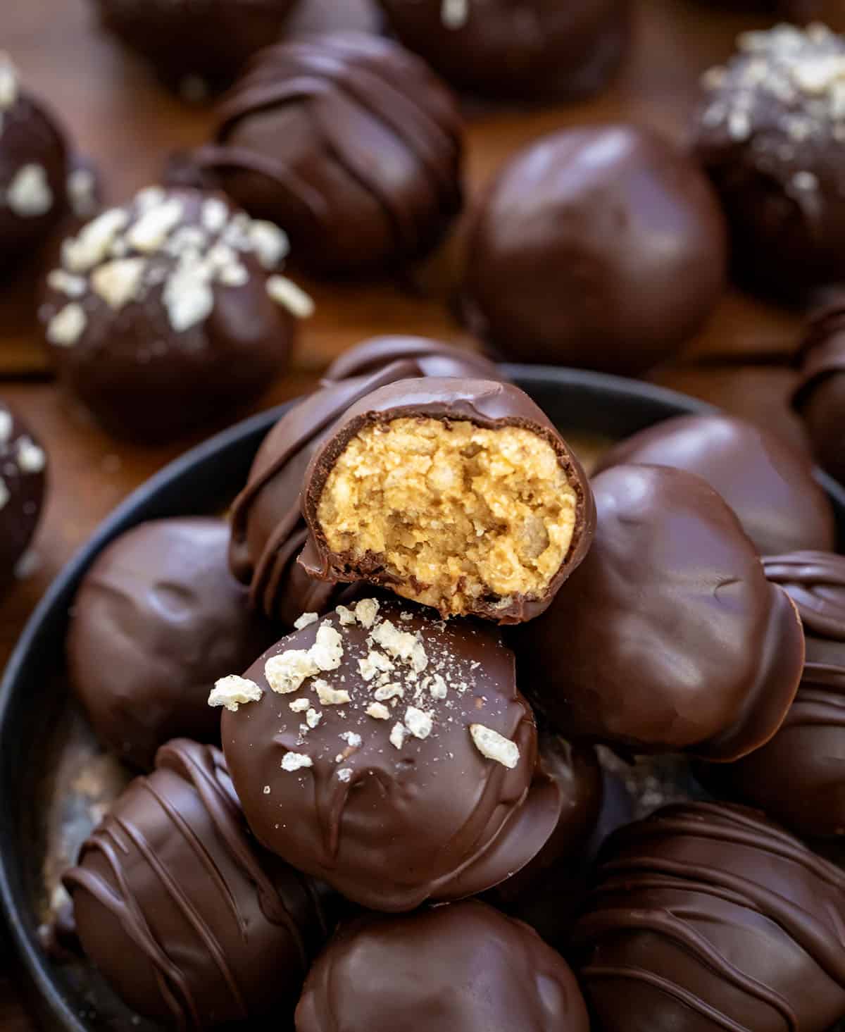 These Peanut Butter Balls with Rice Krispies are sweet, crunchy, and totally irresistible! Creamy peanut butter meets crispy cereal and a rich chocolate coating, making them the perfect treat! Peanut Butter Balls with Rice Krispies on a platter surrounded by more Peanut Butter Balls with Rice Krispies.