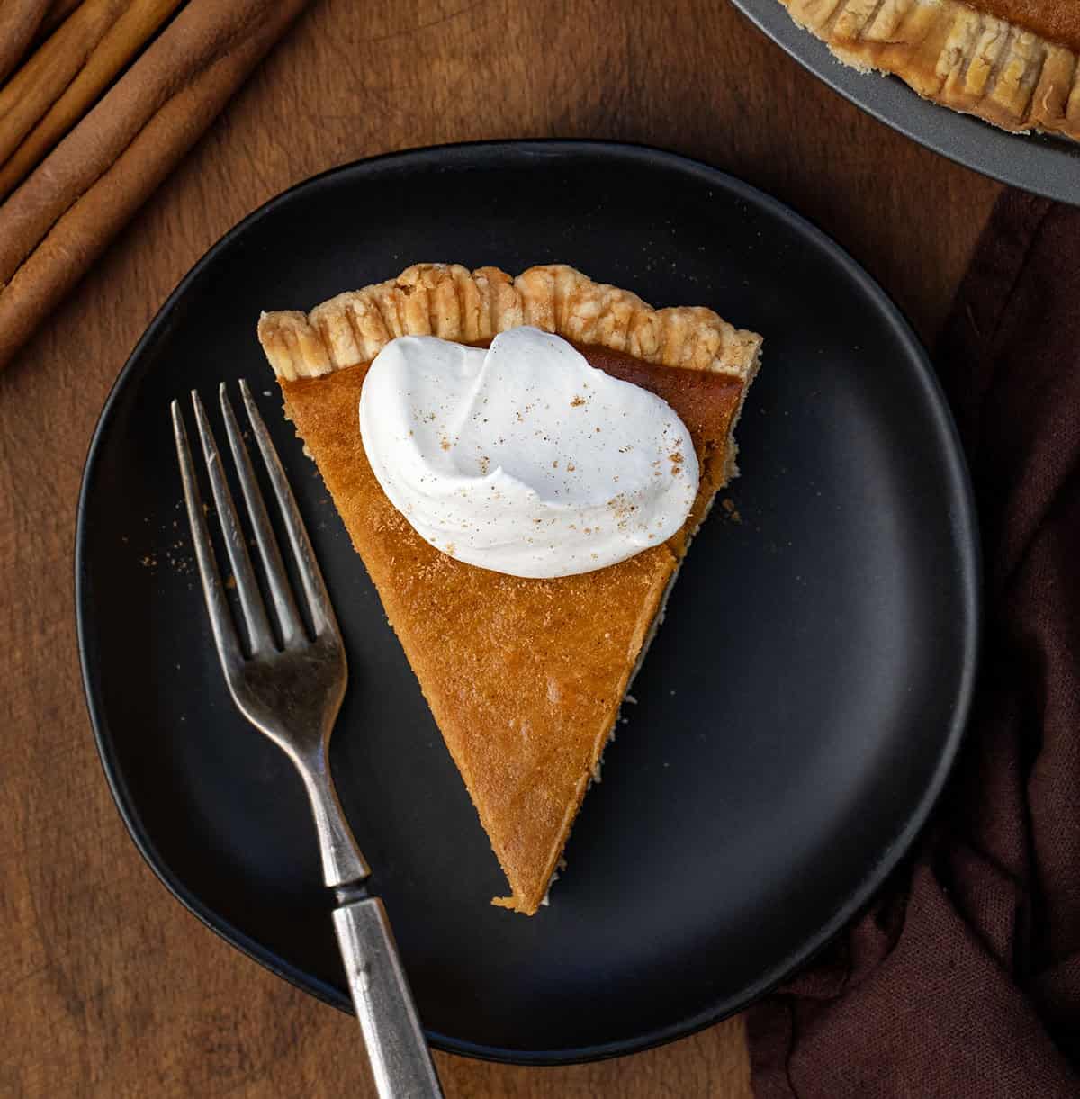 Rich, creamy, and perfectly spiced, this Roasted Sweet Potato Pie elevates the classic holiday dessert with roasted fresh sweet potatoes for deeper flavor! Slice of Roasted Sweet Potato Pie on a black plate with a fork on a wooden table.