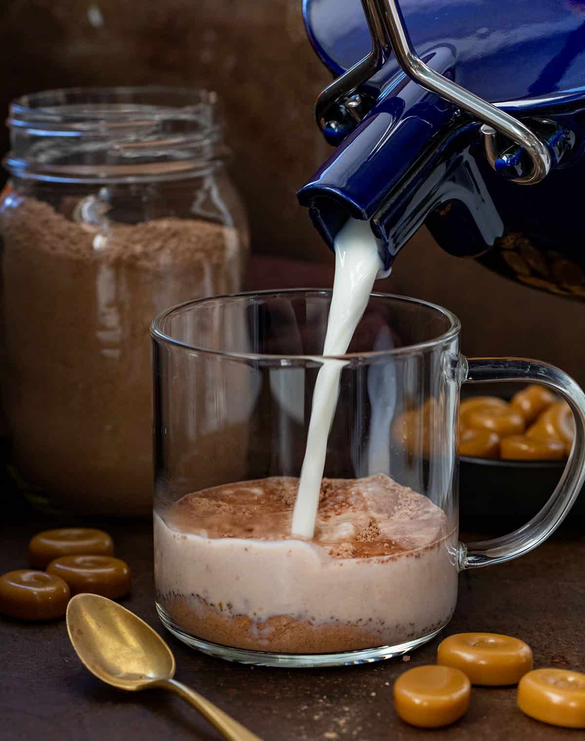 Pouring milk into a glass mug with Salted Caramel Hot Cocoa Mix in it.