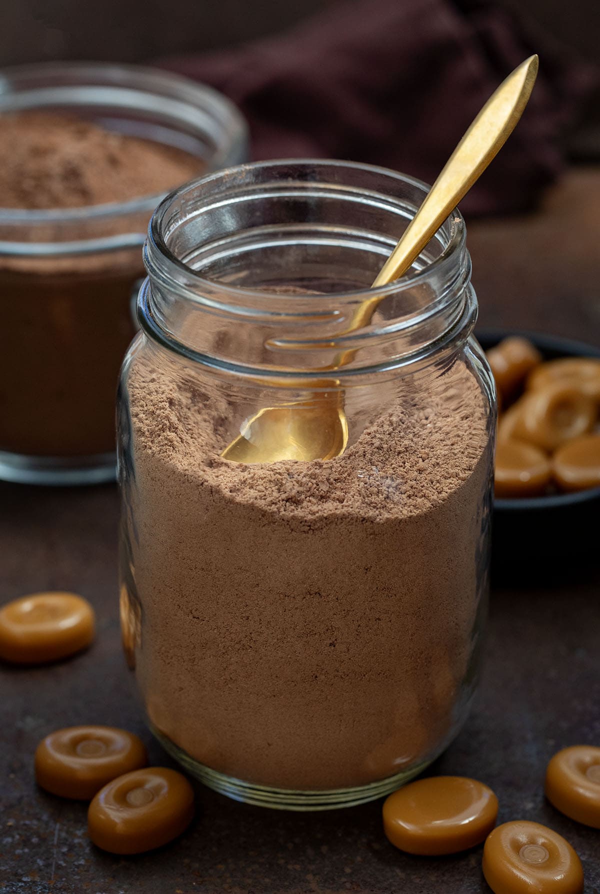 Glass mason jar of Salted Caramel Hot Cocoa Mix with a small golden spoon.