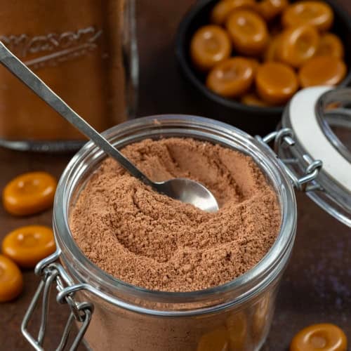 Container of Salted Caramel Hot Cocoa Mix with a spoon in it.