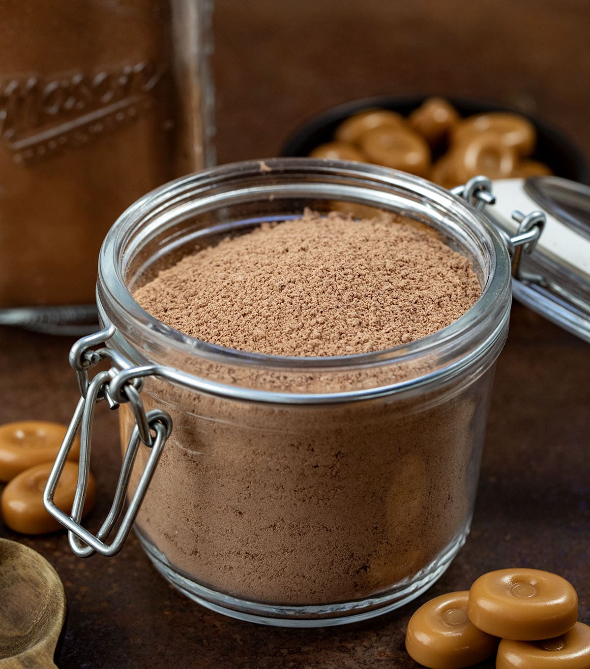 Open container of Salted Caramel Hot Cocoa Mix on a wooden table with Werther's hard caramel candies near it.