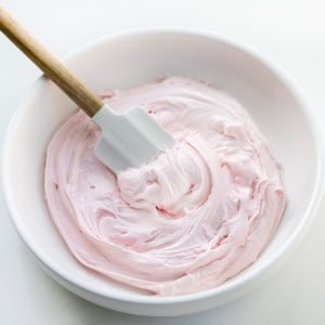 White bowl of Strawberry Marshmallow Frosting with a spatula in it.