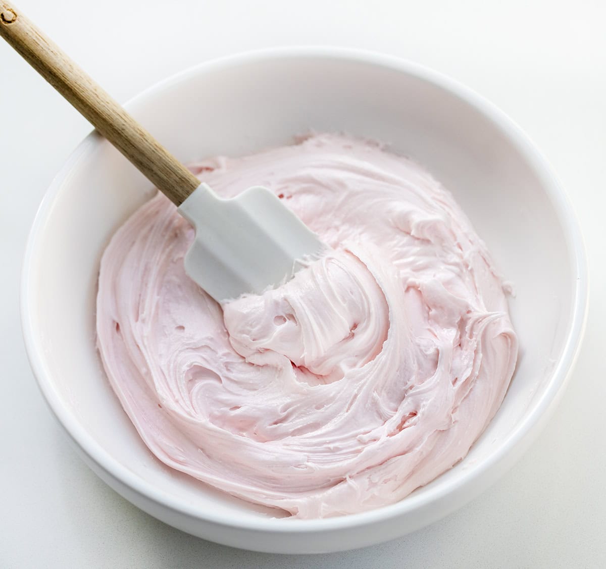 White bowl of Strawberry Marshmallow Frosting with a spatula in it.