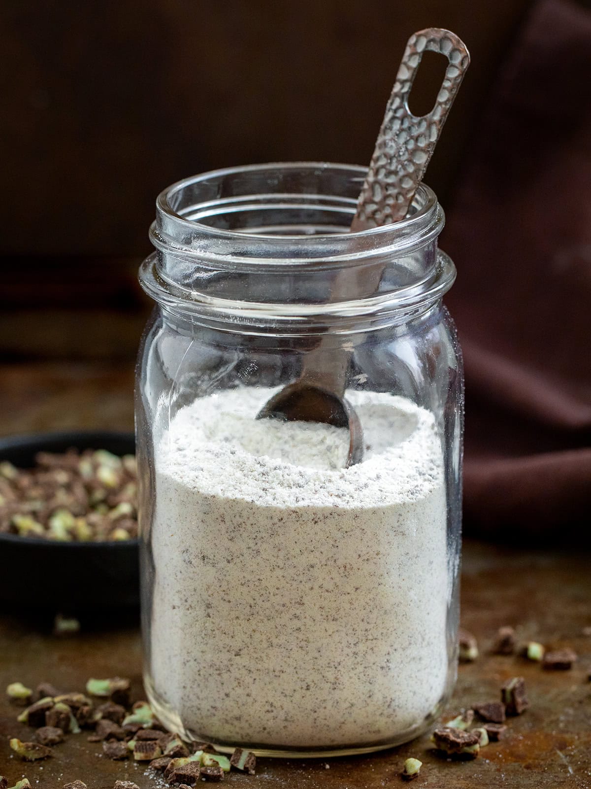 Glass mason jar filled with Andes Hot Cocoa Mix and with a measuring spoon in it.