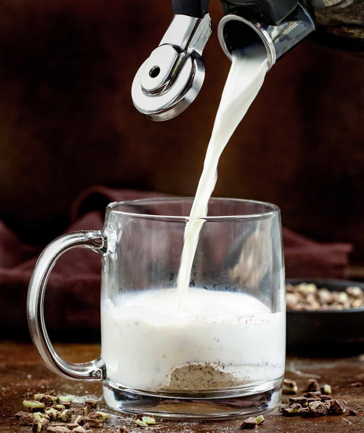 Pouring hot milk into a glass mug of Andes Hot Cocoa Mix.