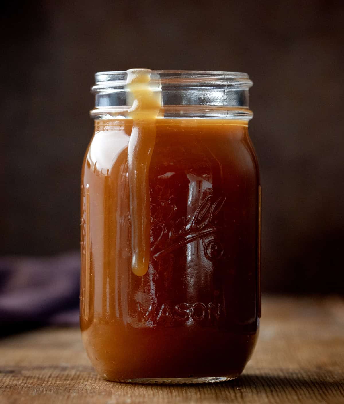 Small glass mason jar of Bourbon Caramel Sauce with some spilling over the side.