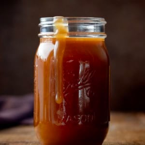 Small glass mason jar of Bourbon Caramel Sauce with some spilling over the side.