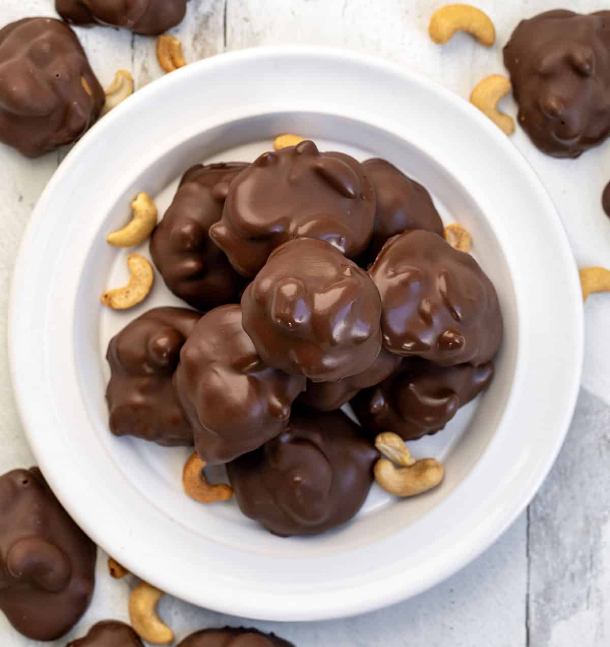Plate of Chocolate Caramel Cashew Clusters on a white table from overhead.