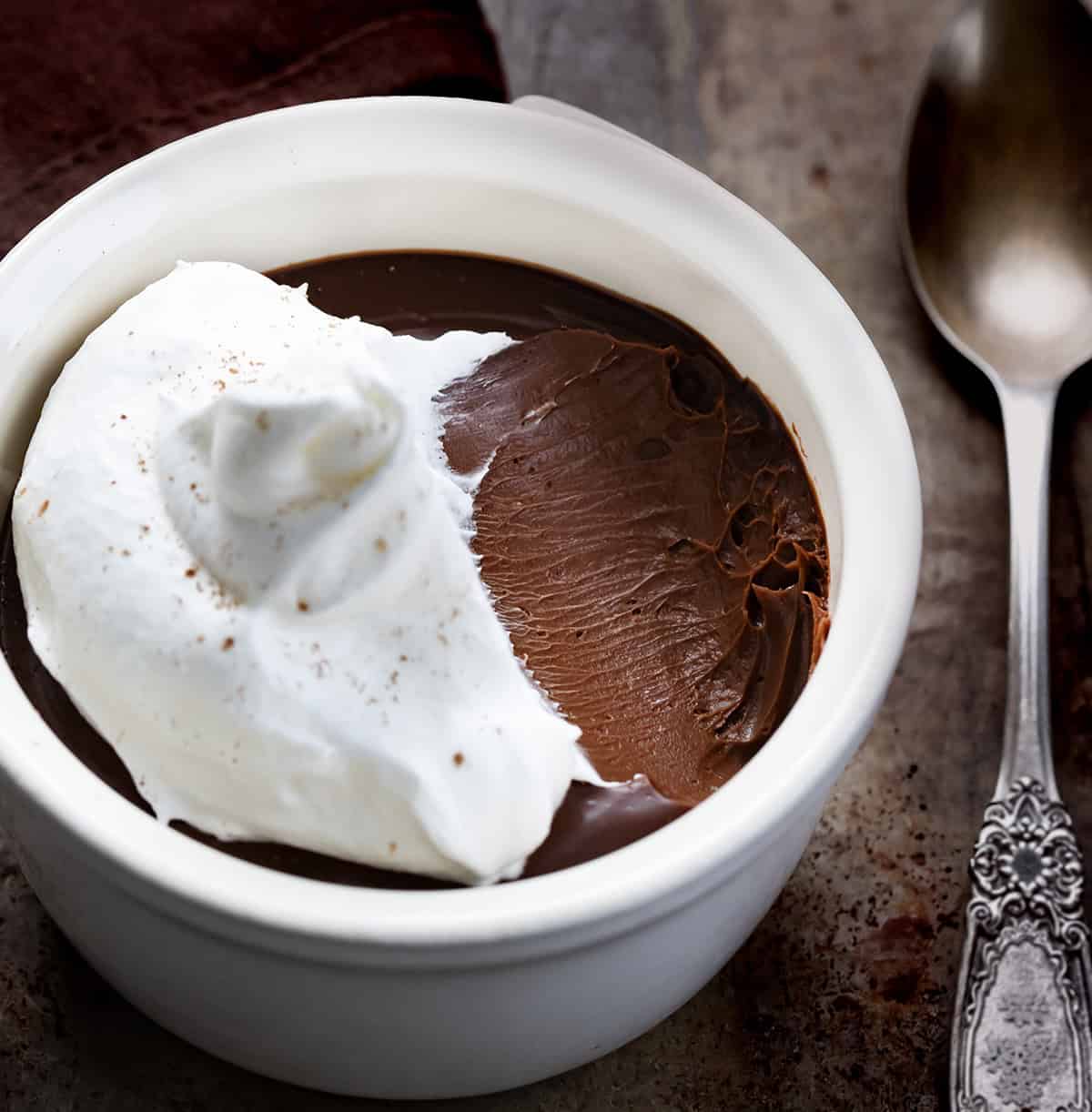 Indulge in Chocolate Pots de Crème, a creamy chocolate custard topped with whipped cream. Perfect for an elegant, easy homemade dessert! Chocolate Pots De Crème with a portion removed showing the creamy texture.
