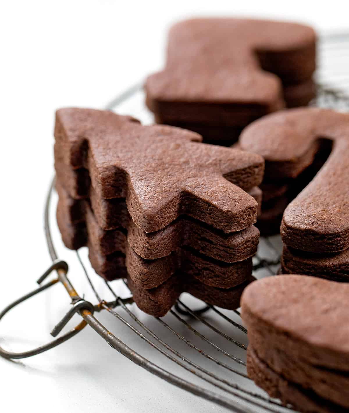 Cut-Out Chocolate Sugar Cookies are soft-centered, rich in cocoa, and hold their shape perfectly for decorating! Stack of Chocolate Sugar Cookie Trees on a cooling rack close up.