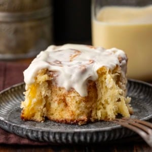 One Eggnog Cinnamon Roll that has a bite removed on a plate.
