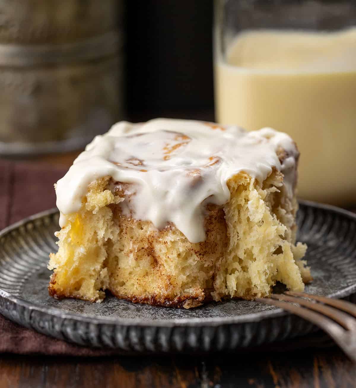 One Eggnog Cinnamon Roll that has a bite removed on a plate.