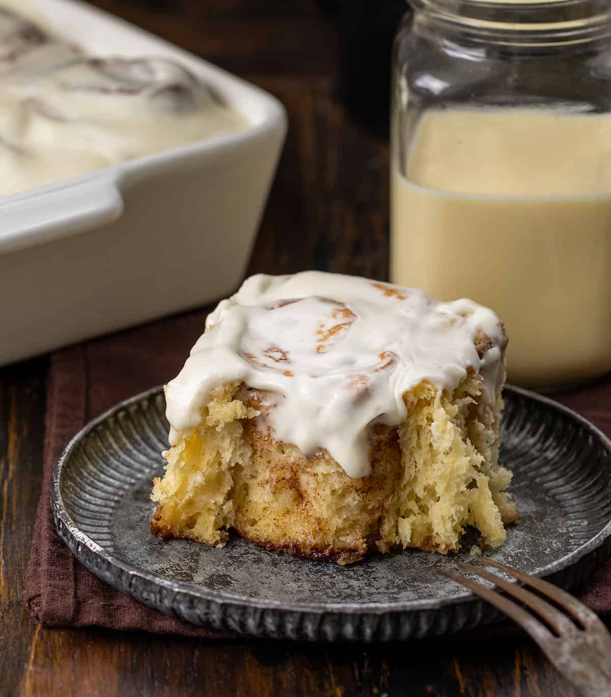 Eggnog Cinnamon Roll on a plate with a bite removed and the fork resting on the plate.