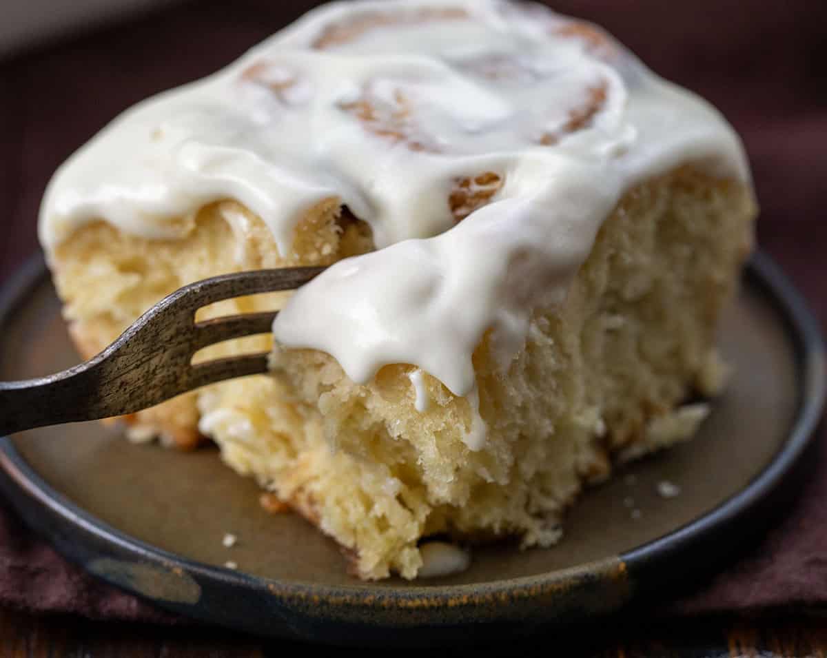 Fork taking a bite of Eggnog Cinnamon Roll on a plate very close up.