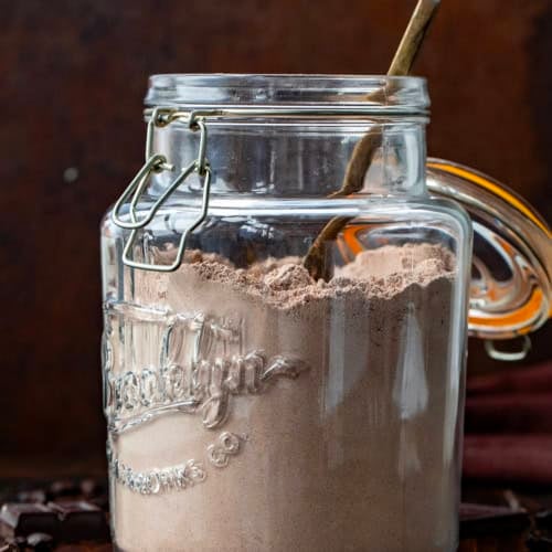 Jar of Mocha Hot Cocoa Mix with a spoon in it on a wooden table.