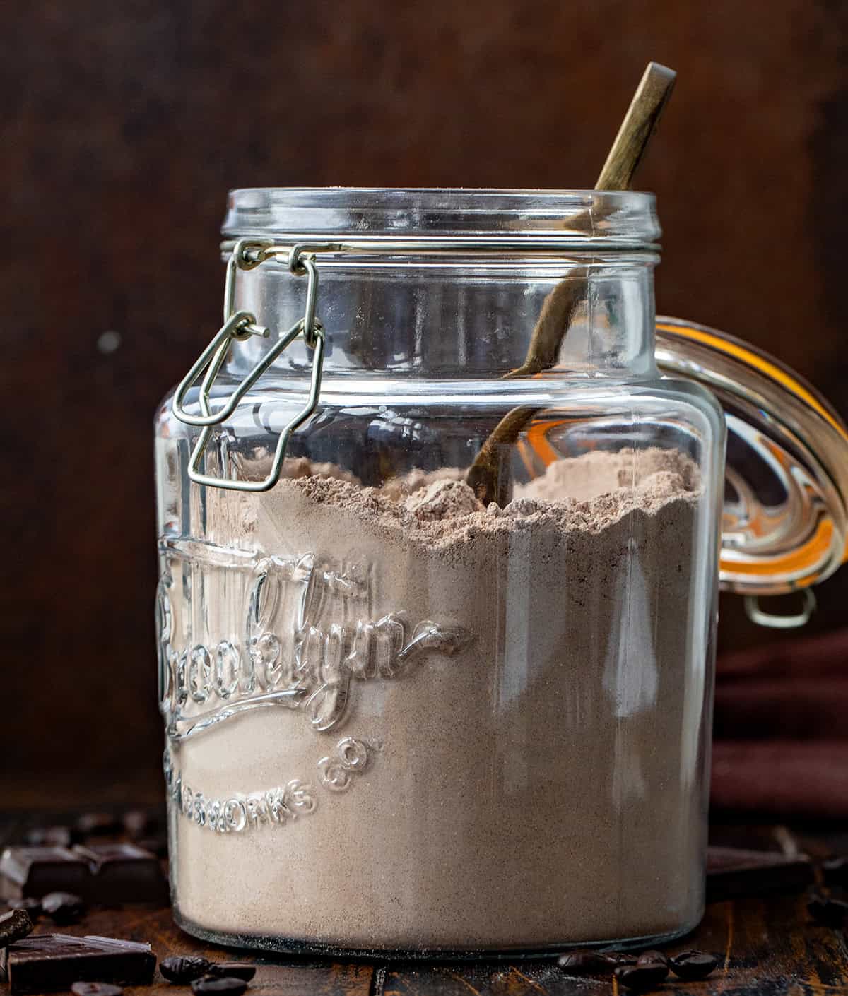 Jar of Mocha Hot Cocoa Mix with a spoon in it on a wooden table.