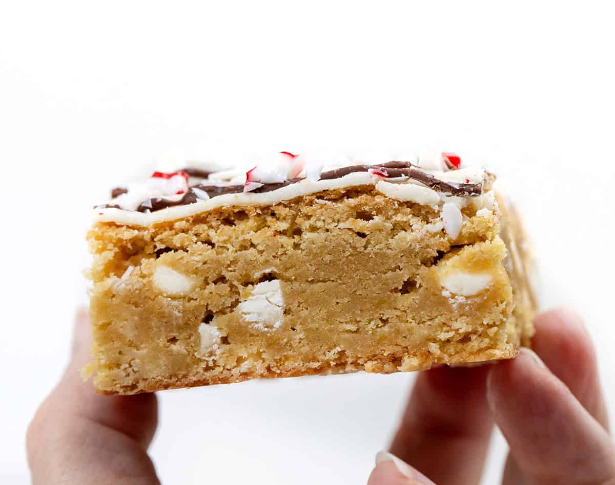 These Peppermint Bark Blondies are rich, buttery, and festive, the perfect holiday treat! The base is my chewy white chocolate blondie, flavored with a touch of peppermint extract. I top each blondie with a double drizzle of milk and white chocolate, then sprinkle on crushed peppermint candies for a holiday-perfect crunch! Hand holding a Peppermint Bark Blondie.